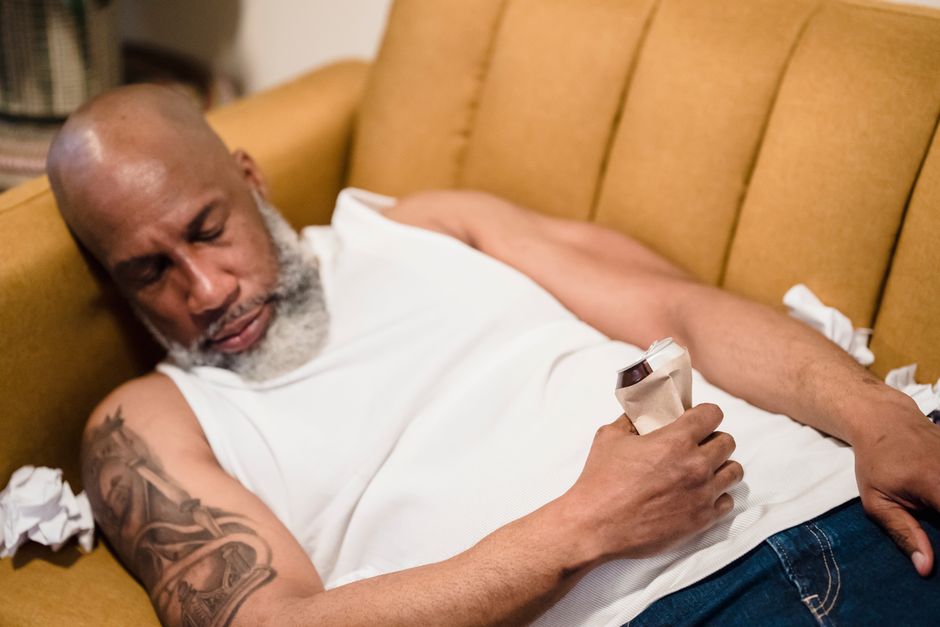 man resting on sofa with ice pack after vasectomy recovery